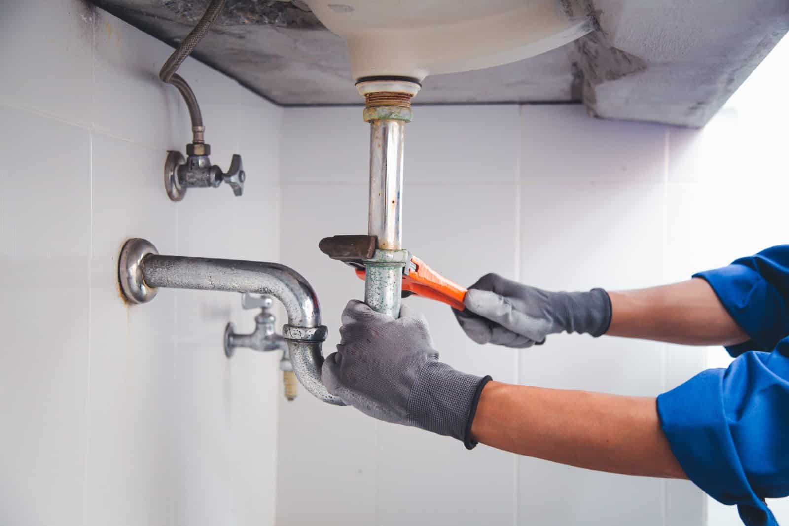 Plumber using a wrench to unclog the drain of the kitchen sink
